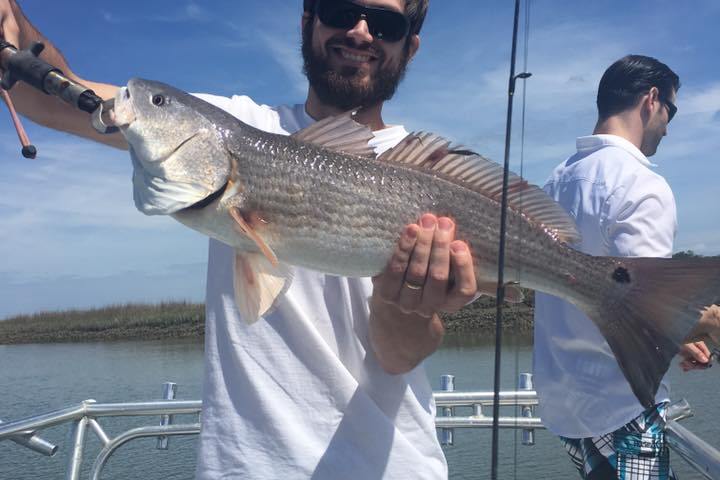 Man standing on boat holding up silver fish he caught