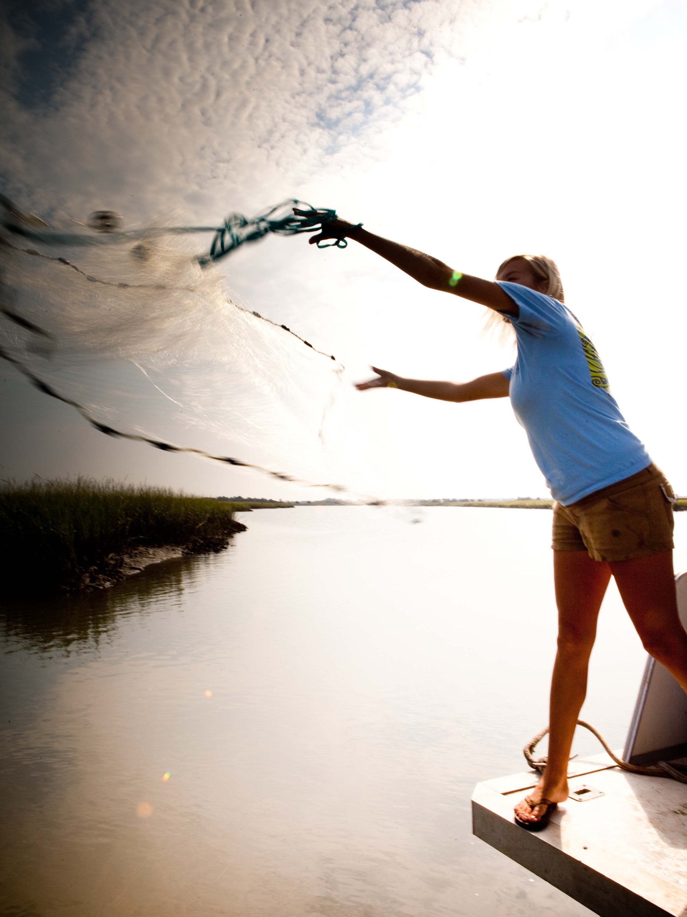 Woman casting a net into water from shore