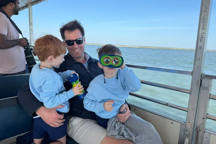 Man and two kids on boat, one child using binoculars, with water view.