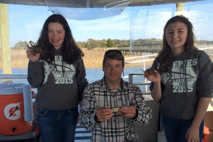 Two kids and a man holding up small blue crabs