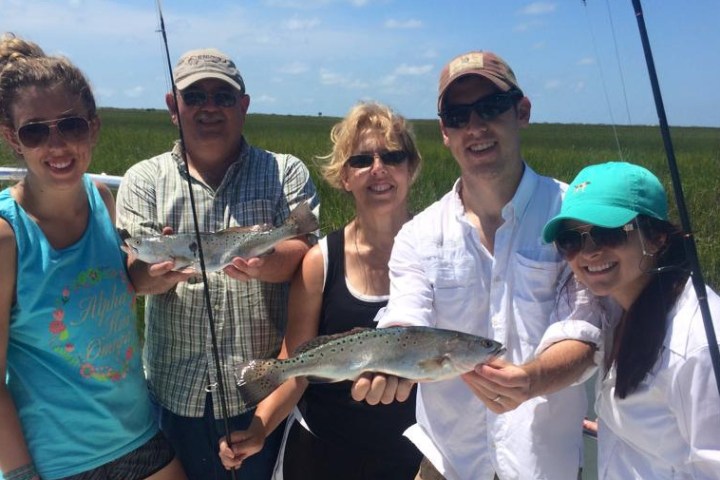 Group of people smiling at camera and holding fish they just caught