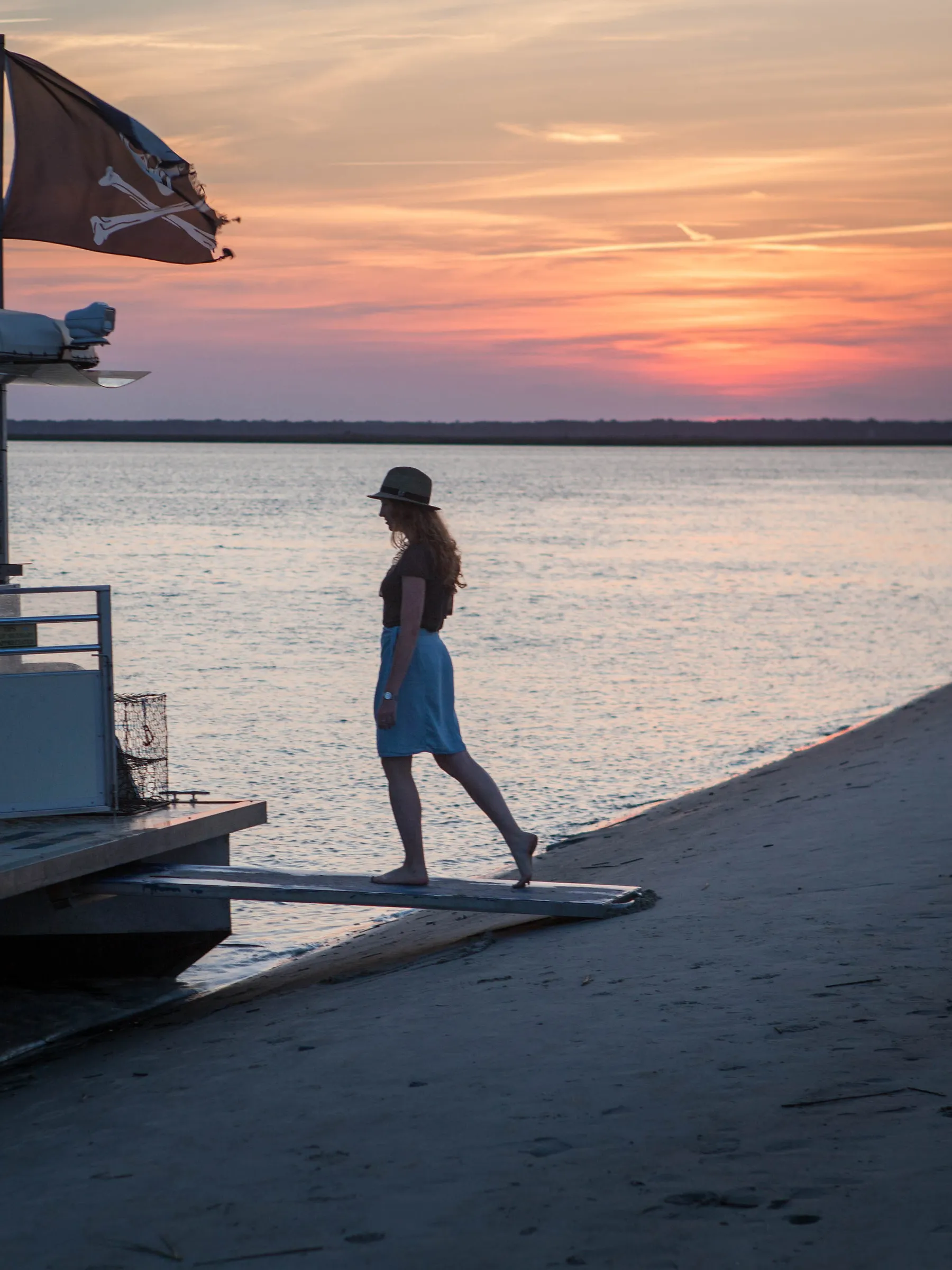 A woman walking up plank to pontoon boat from the beach
