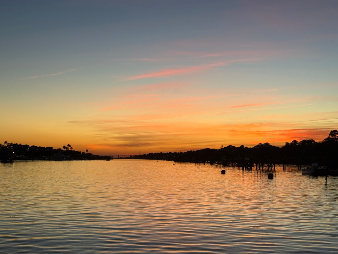 Tranquil sunset over a river with silhouetted trees and vibrant orange sky.