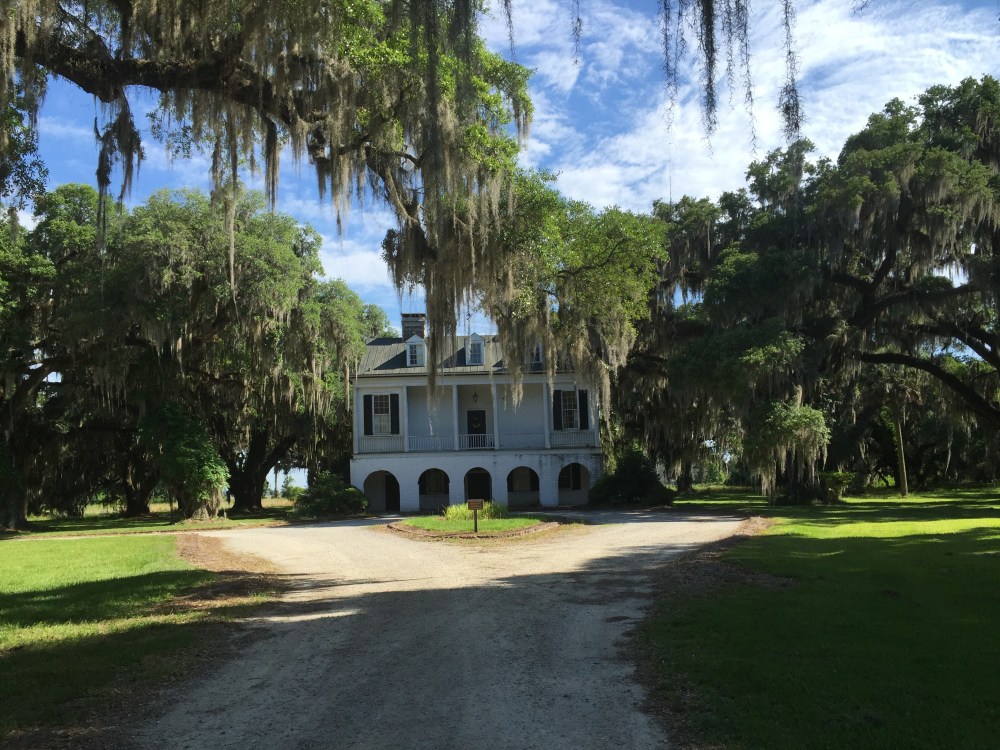 Historic white house framed by oak trees with Spanish moss.