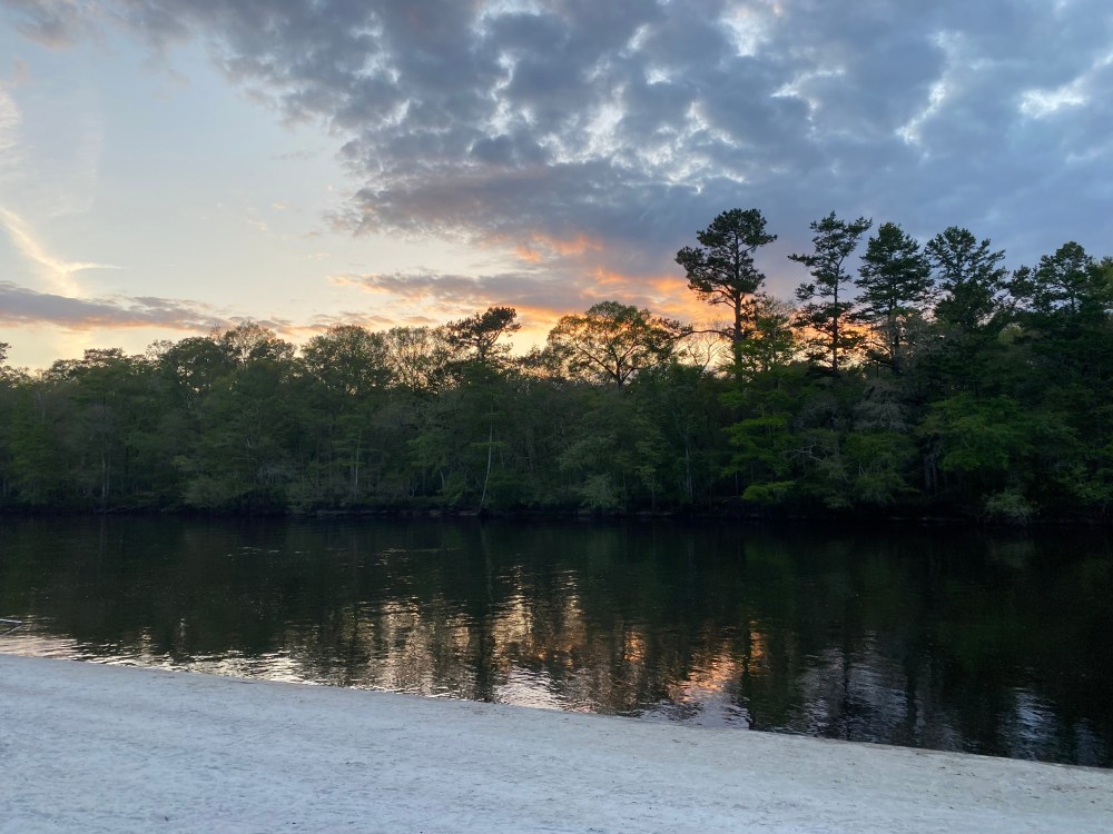 Sunset over a river with trees and clouds in the background.